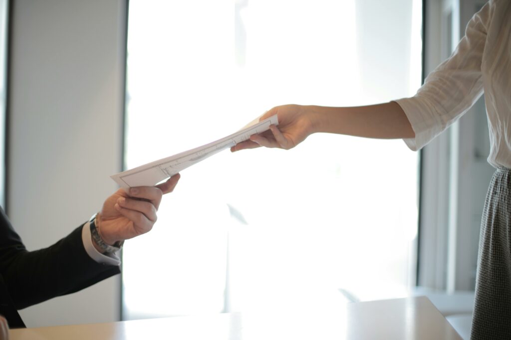 Close-up of hands exchanging documents in a business setting indoors.