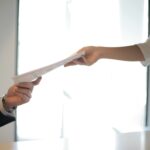 Close-up of hands exchanging documents in a business setting indoors.